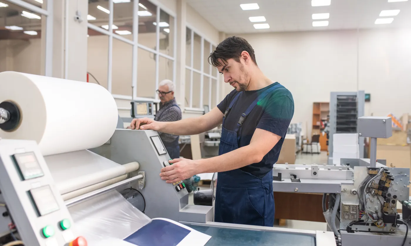 A print technician operating commercial printing and laminating equipment