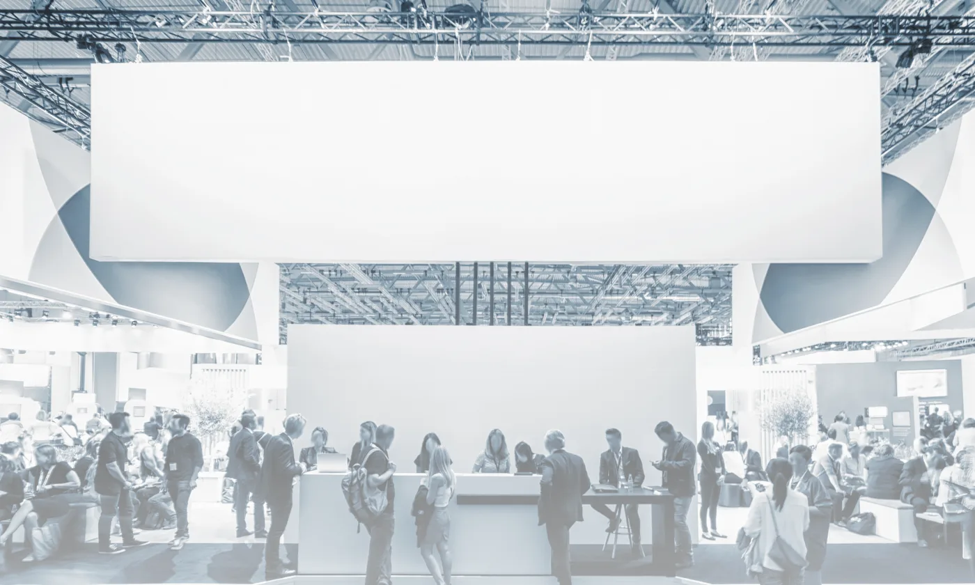 A busy trade show floor with a large overhead booth banner display